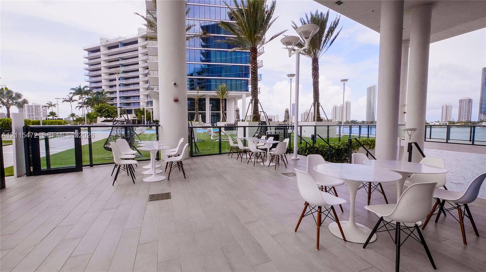 Covered outdoor patio featuring large-format tile flooring, structural pillars, and a glass panel railing system overlooking the water