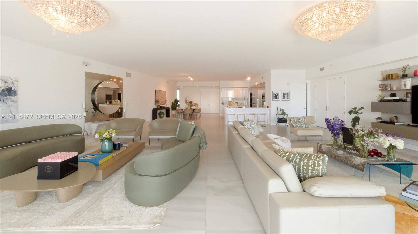 Open-concept interior featuring large-format tile flooring, dual crystal chandeliers, and built-in wall cabinetry