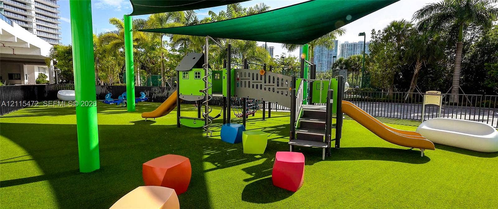 Recreational area featuring a structured play system, synthetic turf surfacing, overhead shade canopy, and perimeter metal fencing