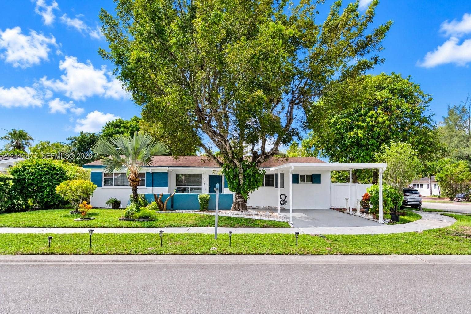 2510 NE 208th Terrace, Miami, FL 33180 Single-story exterior featuring painted stucco siding, a covered carport, manicured lawn, established shade trees, and privacy fencing