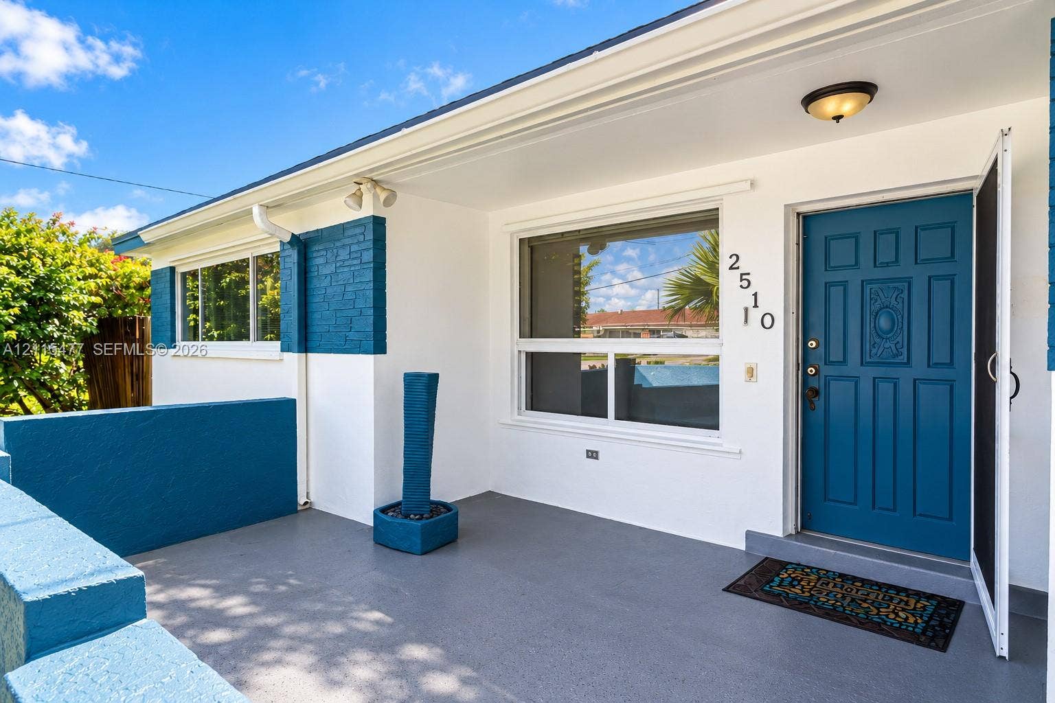 2510 NE 208th Terrace, Miami, FL 33180 Covered entryway with concrete flooring, blue-painted masonry accents, large picture window, and paneled front door
