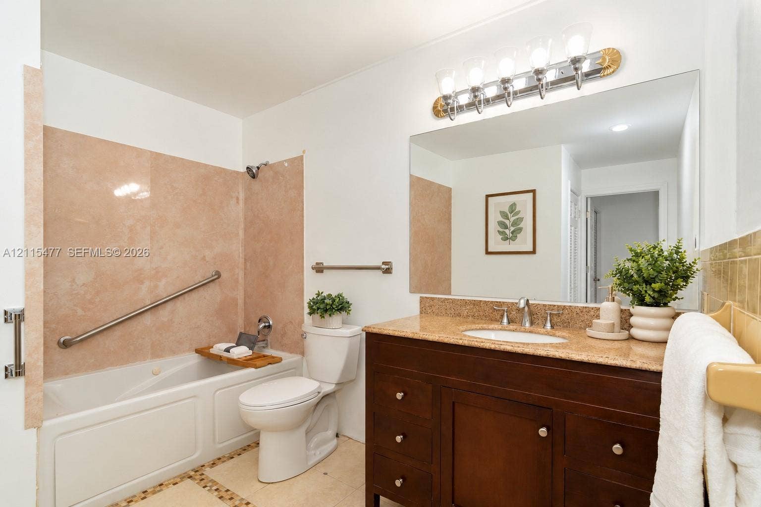 2510 NE 208th Terrace, Miami, FL 33180 Dark wood vanity with a stone countertop, integrated sink, large wall-mounted mirror, five-light vanity fixture, and a tub with stone-tiled surround