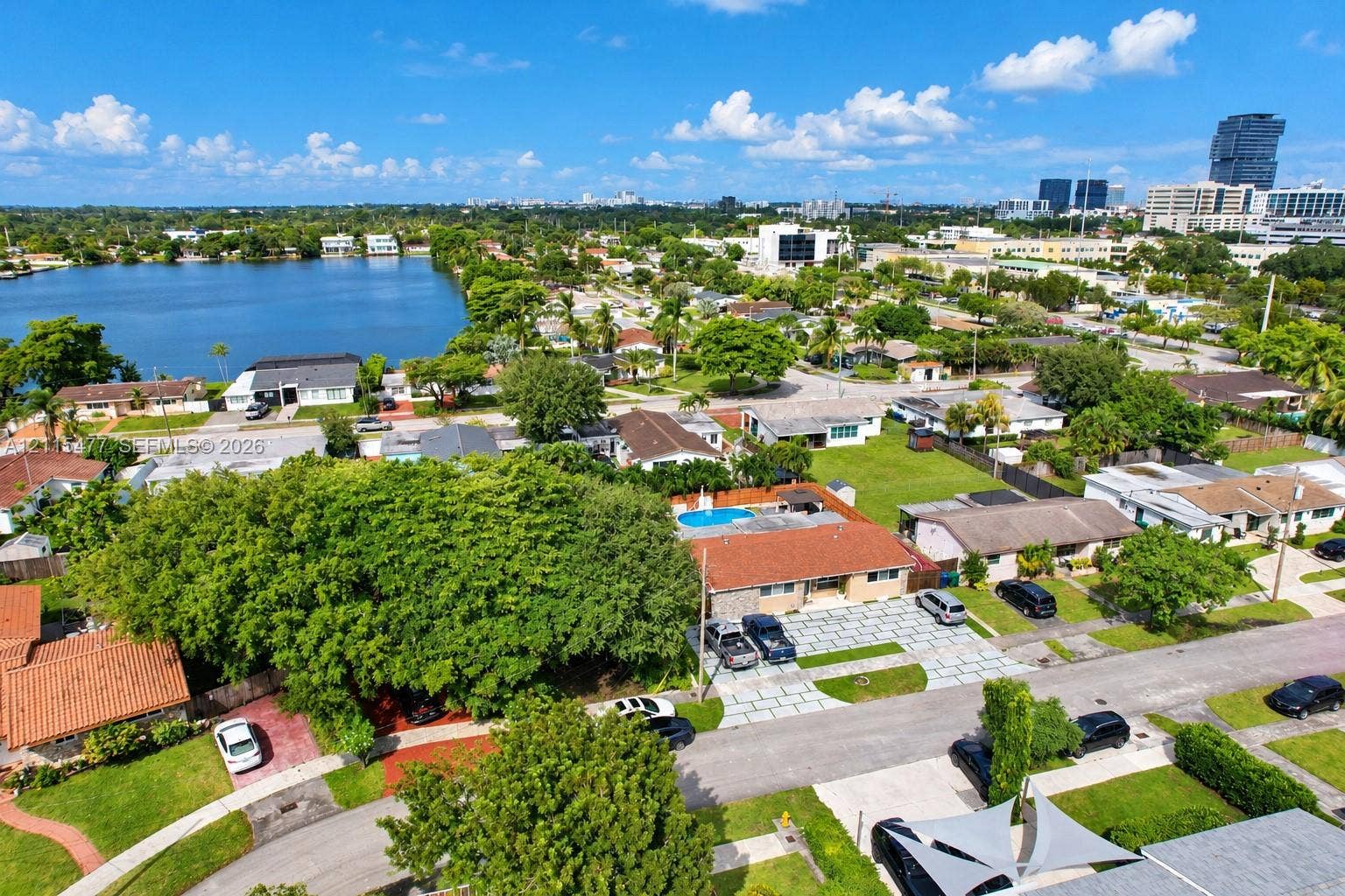 2510 NE 208th Terrace, Miami, FL 33180 Aerial perspective featuring a single-story residence with a red-tiled roof, an inground swimming pool, a multi-vehicle paved driveway, and mature trees situated within an urban residential setting