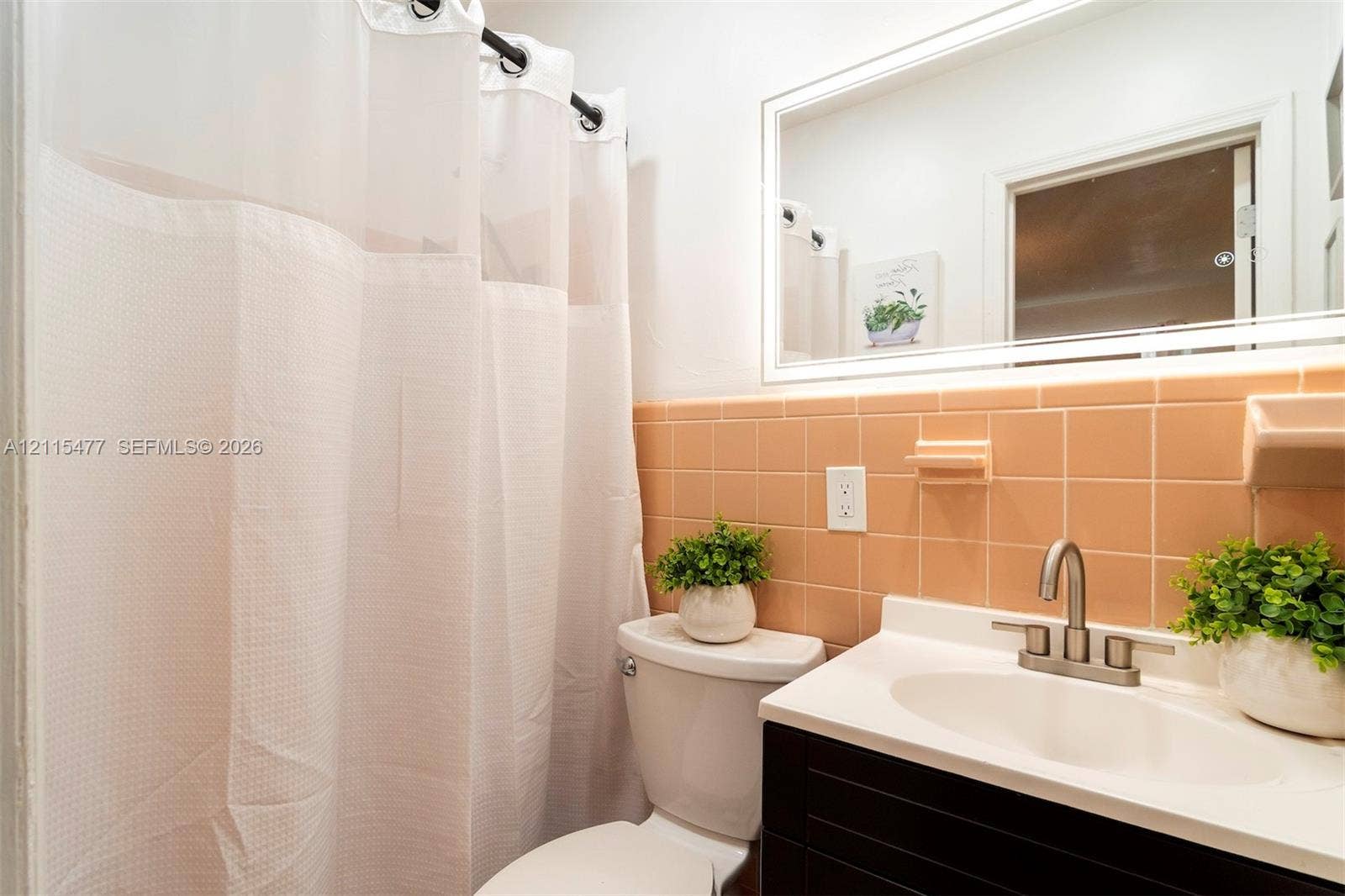 2510 NE 208th Terrace, Miami, FL 33180 Bathroom featuring a dark-finish vanity with a white integrated sink, ceramic wall tiling, a wall-mounted mirror, and brushed-nickel faucet hardware