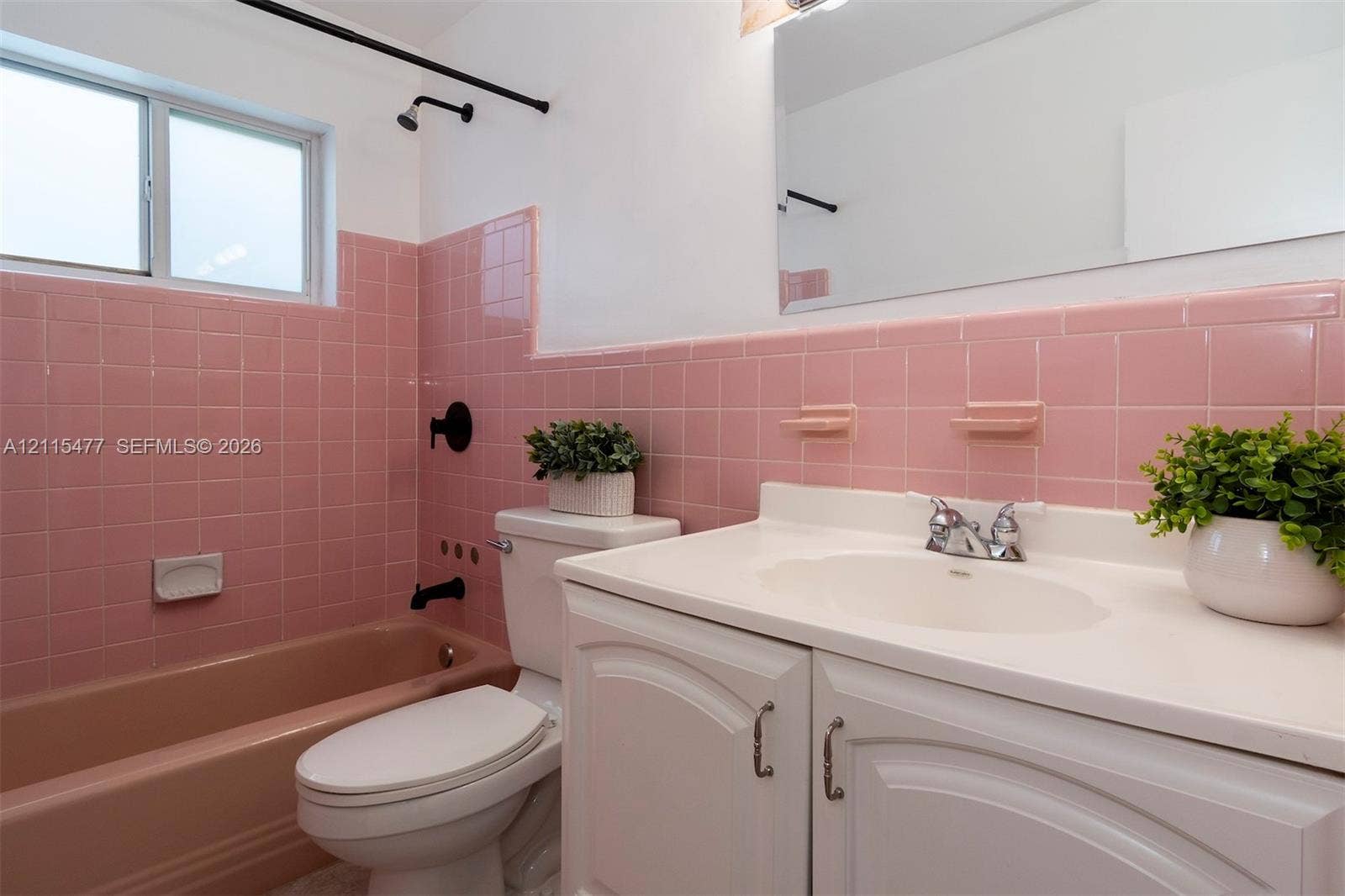 2510 NE 208th Terrace, Miami, FL 33180 Bathroom featuring pink tile wall surround, integrated bathtub, white vanity with molded countertop, chrome dual-handle faucet, and black matte shower fixtures