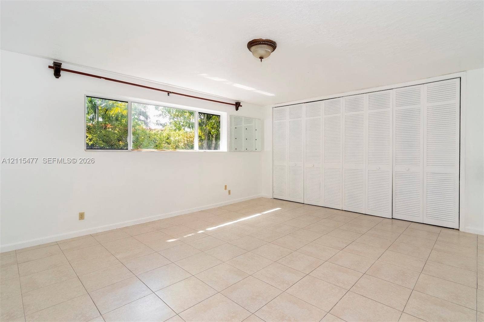2510 NE 208th Terrace, Miami, FL 33180 Room featuring neutral tile flooring, expansive wall-to-wall louvered-panel closets, and a large rectangular window with a window rod and finials