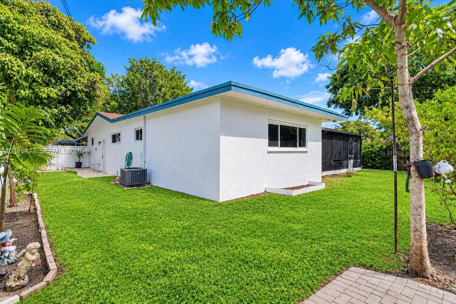 2510 NE 208th Terrace, Miami, FL 33180 Exterior of the home featuring a white stucco facade, flat roofline, integrated screened-in enclosure, and expansive lawn with stone paver hardscaping