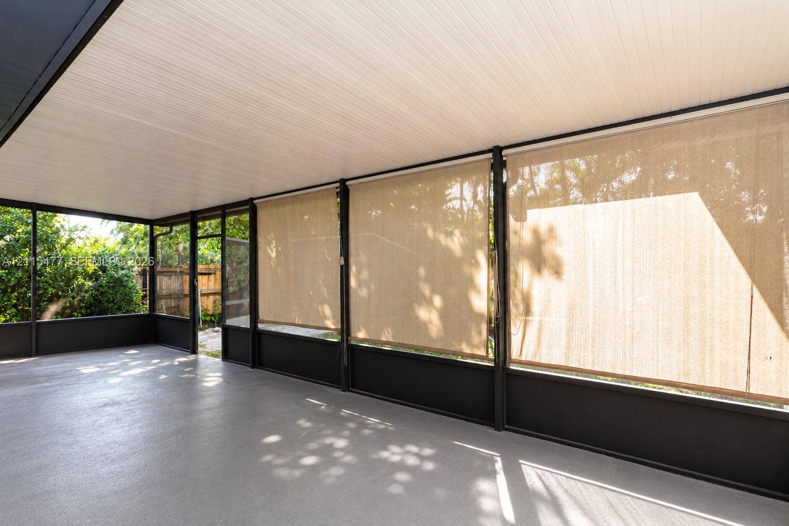 2510 NE 208th Terrace, Miami, FL 33180 Screened-in porch featuring a solid roof, neutral concrete flooring, dark metal framework, and retractable sun shades