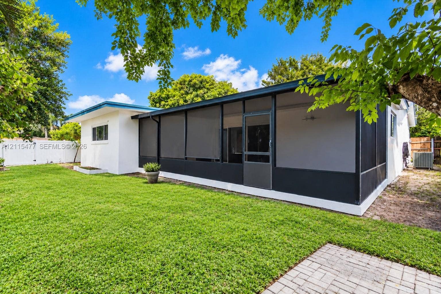 2510 NE 208th Terrace, Miami, FL 33180 Backyard featuring a screened-in lanai, manicured lawn, paver patio, and white perimeter fencing