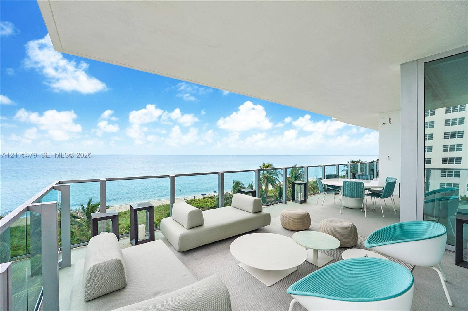 Expansive covered balcony featuring a glass panel railing, neutral-toned flooring, and direct oceanfront positioning