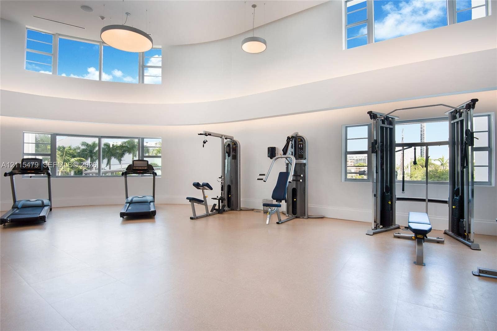 Expansive fitness area featuring soaring curved ceilings, multi-level oversized windows, recessed perimeter lighting, and neutral large-format tile flooring