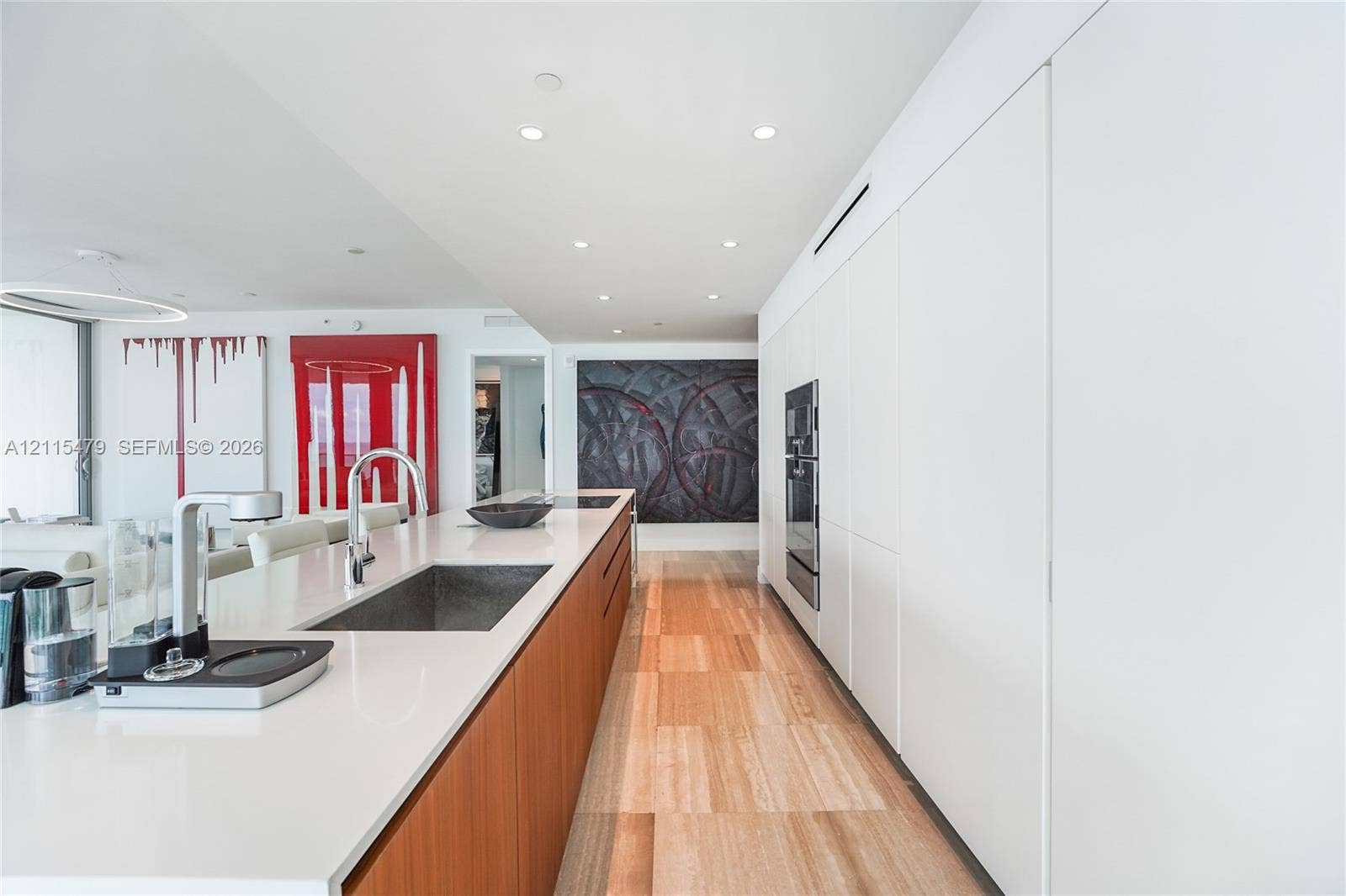 Kitchen featuring a central island with a quartz countertop, integrated sink, wood-finish cabinetry, floor-to-ceiling white paneled wall storage, and recessed lighting