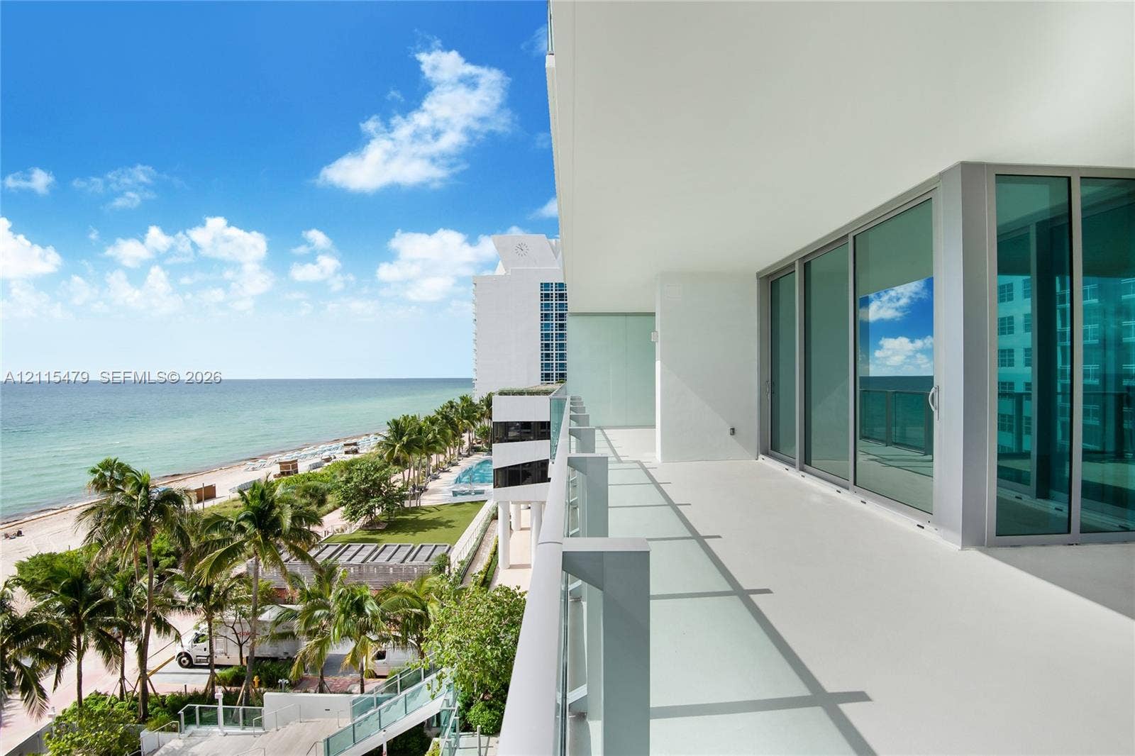 Covered balcony with a glass panel railing, expansive floor-to-ceiling glass sliding doors, and direct exposure to coastal scenery