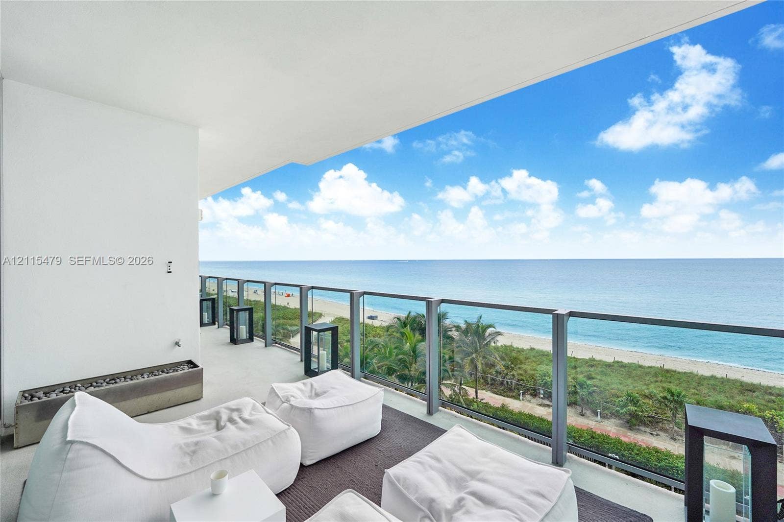 Covered balcony featuring a glass and metal railing, concrete flooring, and an integrated stone-filled fire feature