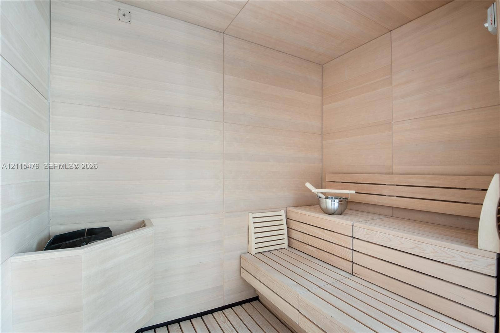 Sauna featuring light-toned wood wall paneling, tiered slatted wood bench seating, and a corner-mounted heater unit