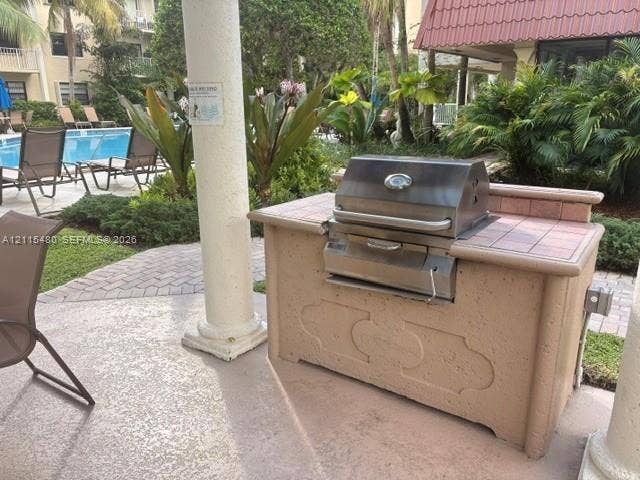 9301 SW 92nd Avenue, #A418, Miami, Miami, FL 33176 Outdoor kitchen station with a stainless steel built-in grill and tile-surround countertop, situated on a textured concrete patio with decorative column support