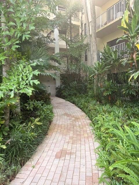 9301 SW 92nd Avenue, #A418, Miami, Miami, FL 33176 Brick-paved walkway bordered by mature tropical landscaping and established trees, featuring tiered balcony structures with vertical railing systems