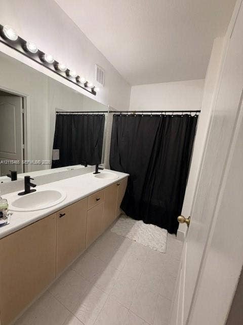 14973 SW 9th Terrace, Miami, Miami, FL 33194 Dual-sink vanity featuring a light-toned wood-finish cabinetry, solid-surface countertop with integrated oval basins, matte black plumbing fixtures, and a large-scale vanity mirror with multi-bulb overhead lighting