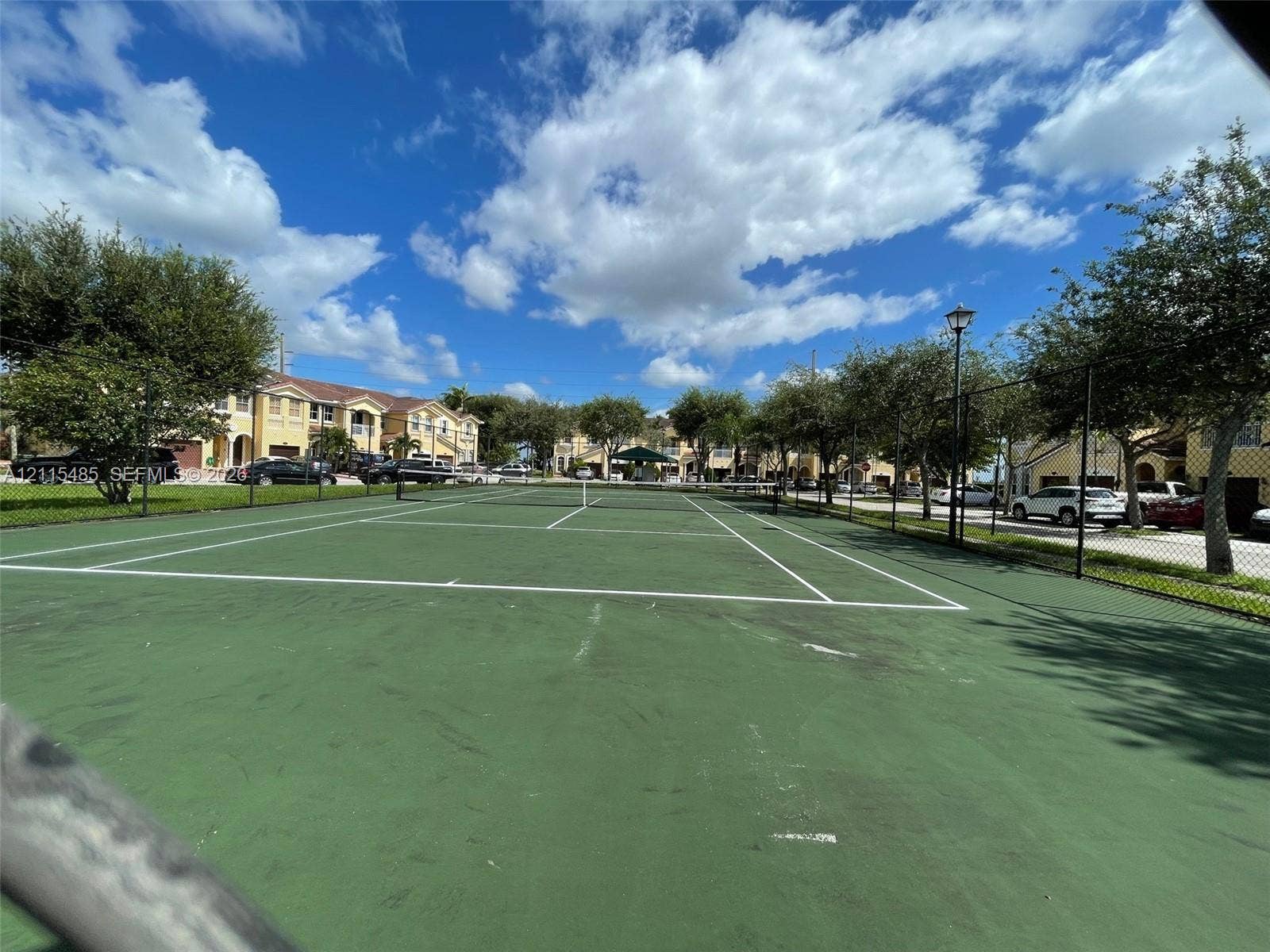14973 SW 9th Terrace, Miami, Miami, FL 33194 Hard-court tennis facility featuring a high-tension perimeter fence, painted court markings, and integrated post lighting