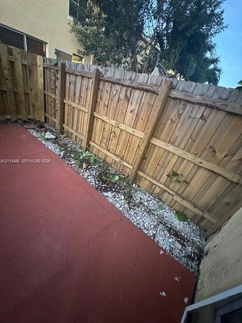 14973 SW 9th Terrace, Miami, Miami, FL 33194 Private outdoor space featuring a red-toned concrete patio, bordered by decorative white gravel, and enclosed by a wood-plank privacy fence