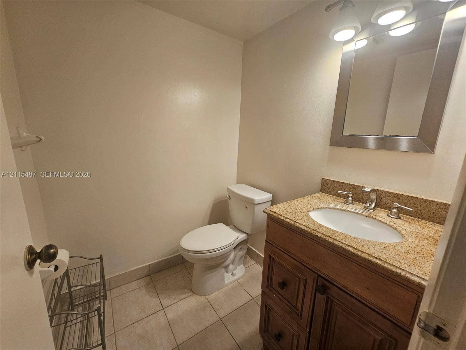 4279 NW 89th Avenue, #205, Coral Springs, Coral Springs, FL 33065 Bathroom featuring a wood-finish vanity with a stone-composite countertop, undermount sink, three-light wall-mounted fixture, and tile flooring