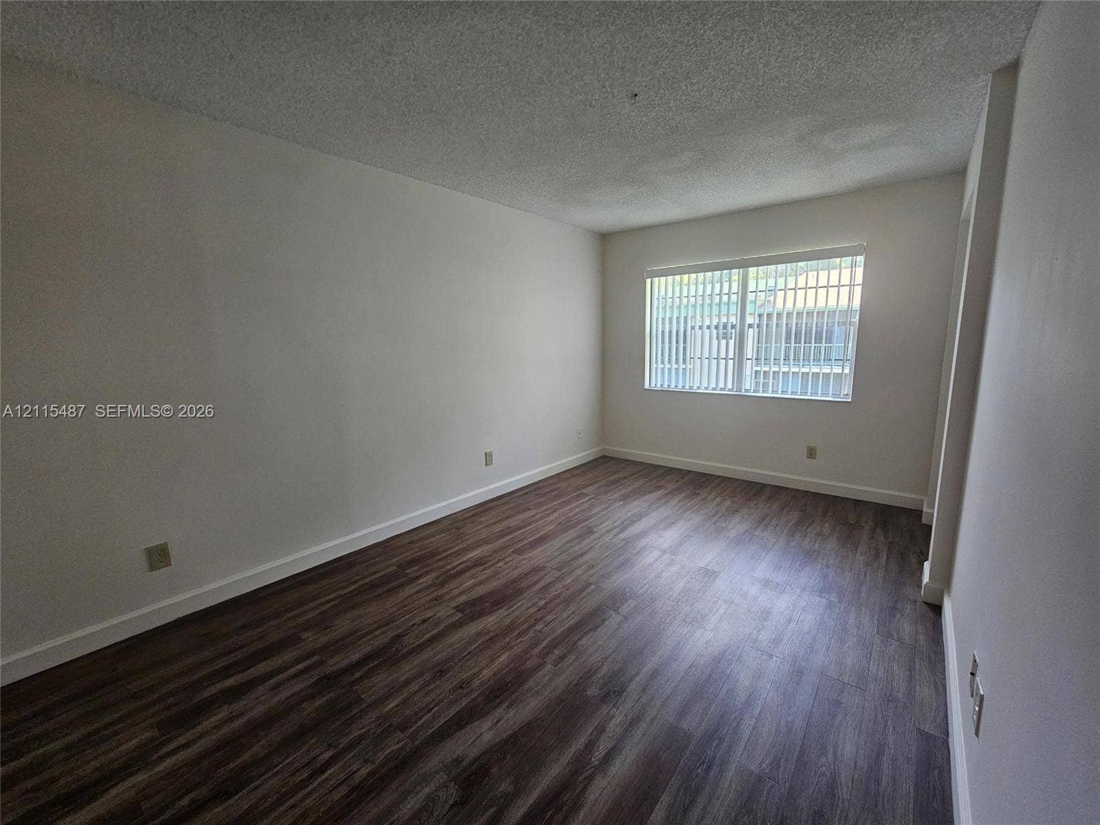 4279 NW 89th Avenue, #205, Coral Springs, Coral Springs, FL 33065 Neutral-toned interior space featuring dark wood-finish flooring, white walls, and a window with horizontal blinds