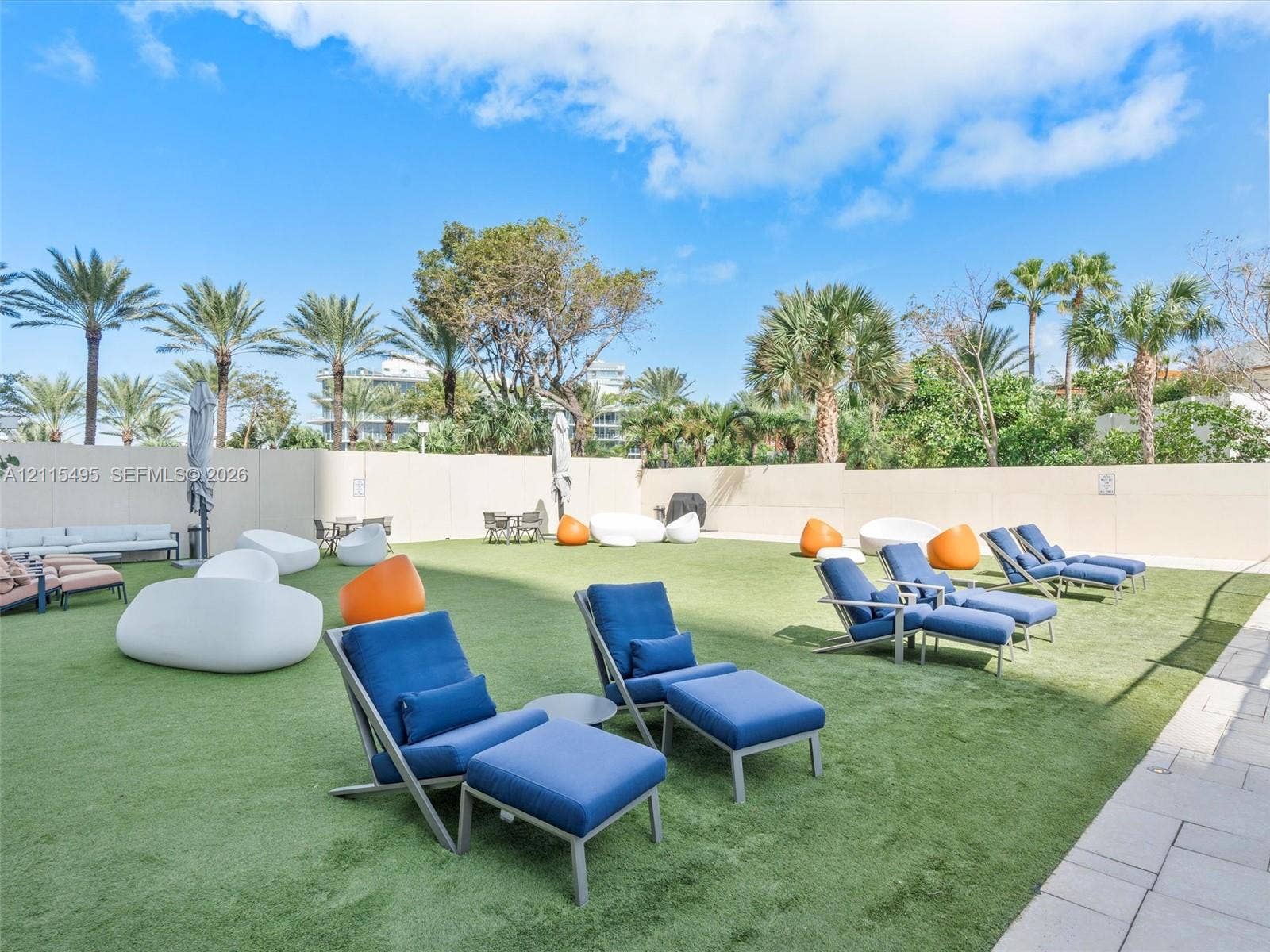 Expansive outdoor recreation space featuring artificial turf, perimeter concrete walls, and mature palm trees