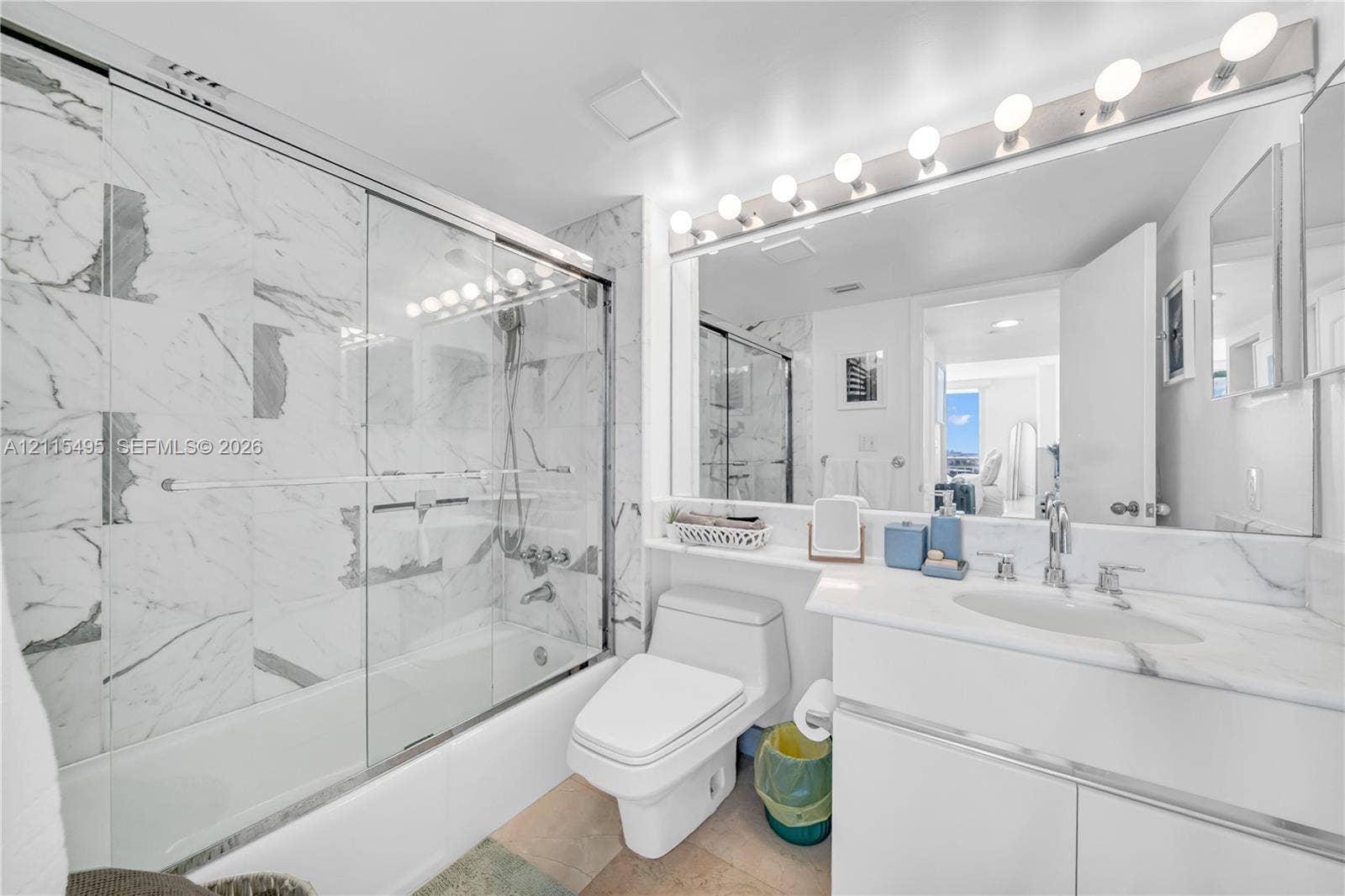 Bathroom featuring a glass-enclosed tub and shower combination with large-format stone-patterned wall tile, white cabinetry with a stone countertop, an integrated oval sink, and a full-width vanity mirror with integrated lighting