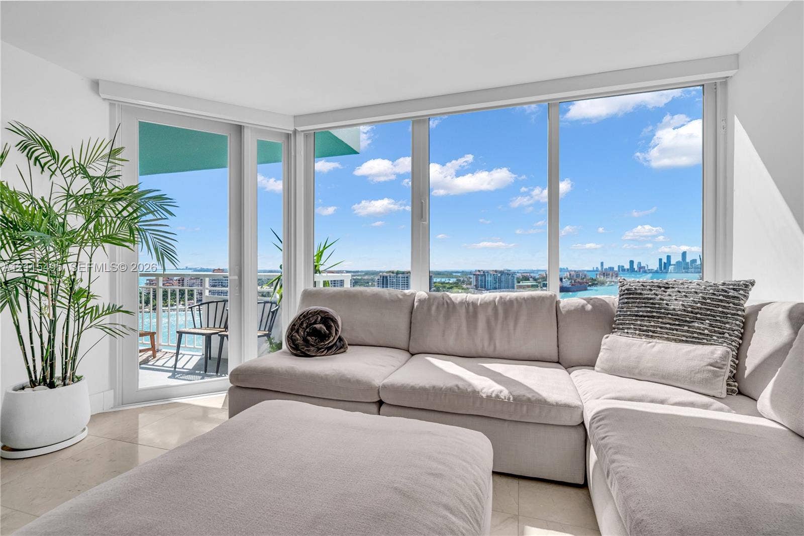 Floor-to-ceiling windows, porcelain tile flooring, and a glass-paneled exterior door opening to a private balcony with panoramic coastal and cityscape horizons