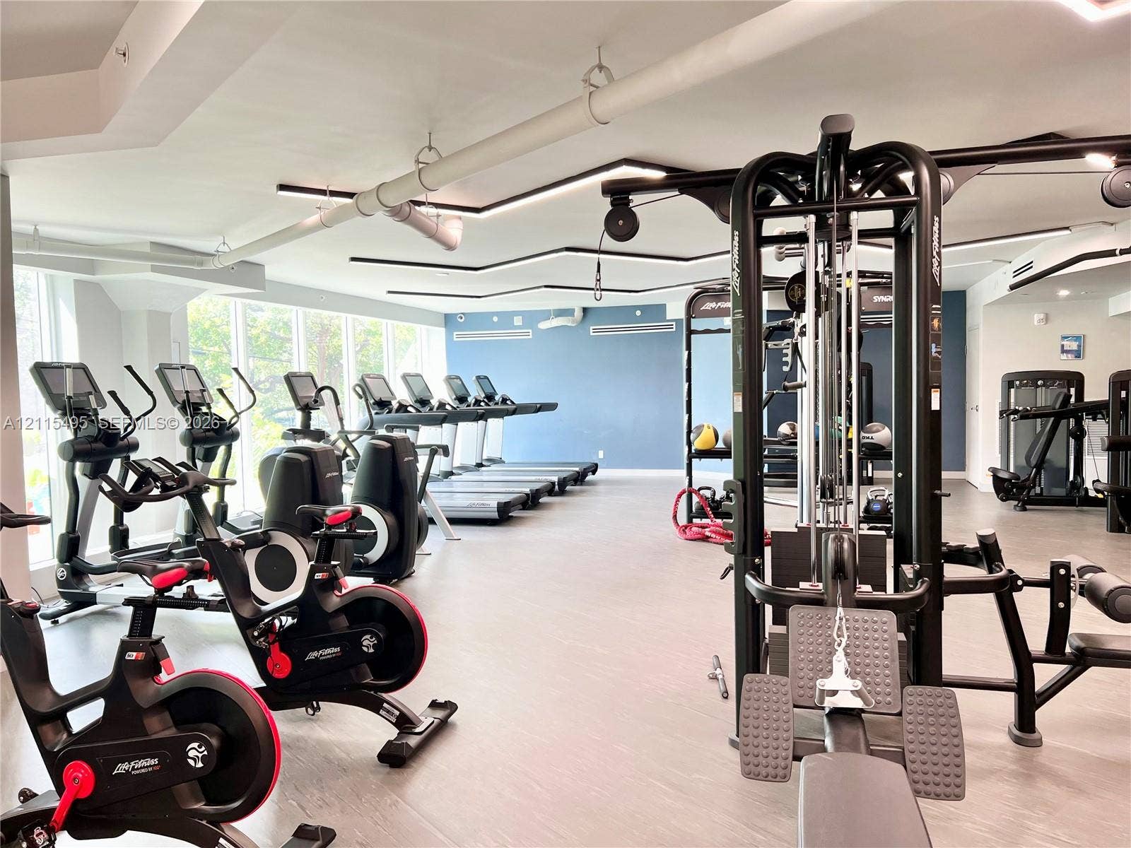 Fitness facility featuring floor-to-ceiling windows, modern recessed geometric ceiling lighting, and smooth-finish flooring