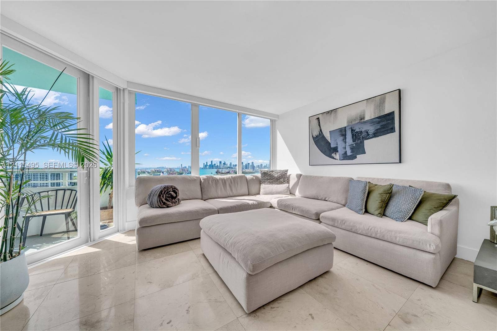 Floor-to-ceiling windows featuring panoramic city and water scenery, neutral stone-finish tile flooring, and access to an exterior balcony
