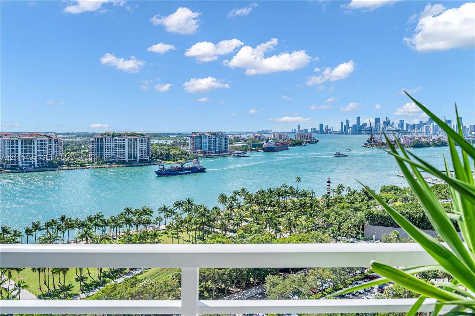 Elevated balcony featuring a white metal railing, overlooking the waterway, coastal greenery, and city skyline