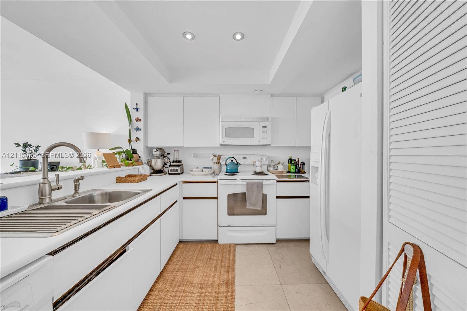 Kitchen featuring white cabinetry with integrated hardware, white appliances, recessed ceiling lighting, a pass-through counter, and a stainless steel sink with a high-arch faucet