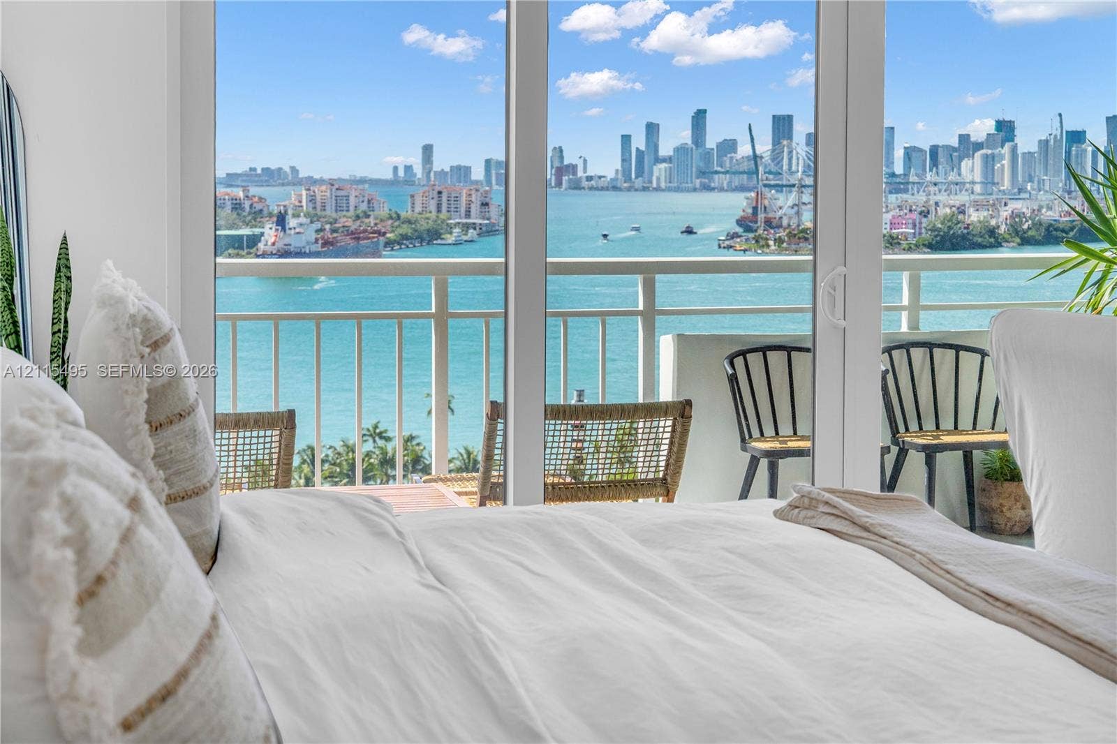 Floor-to-ceiling sliding glass doors opening to a private balcony with railing, featuring a coastal and urban skyline backdrop