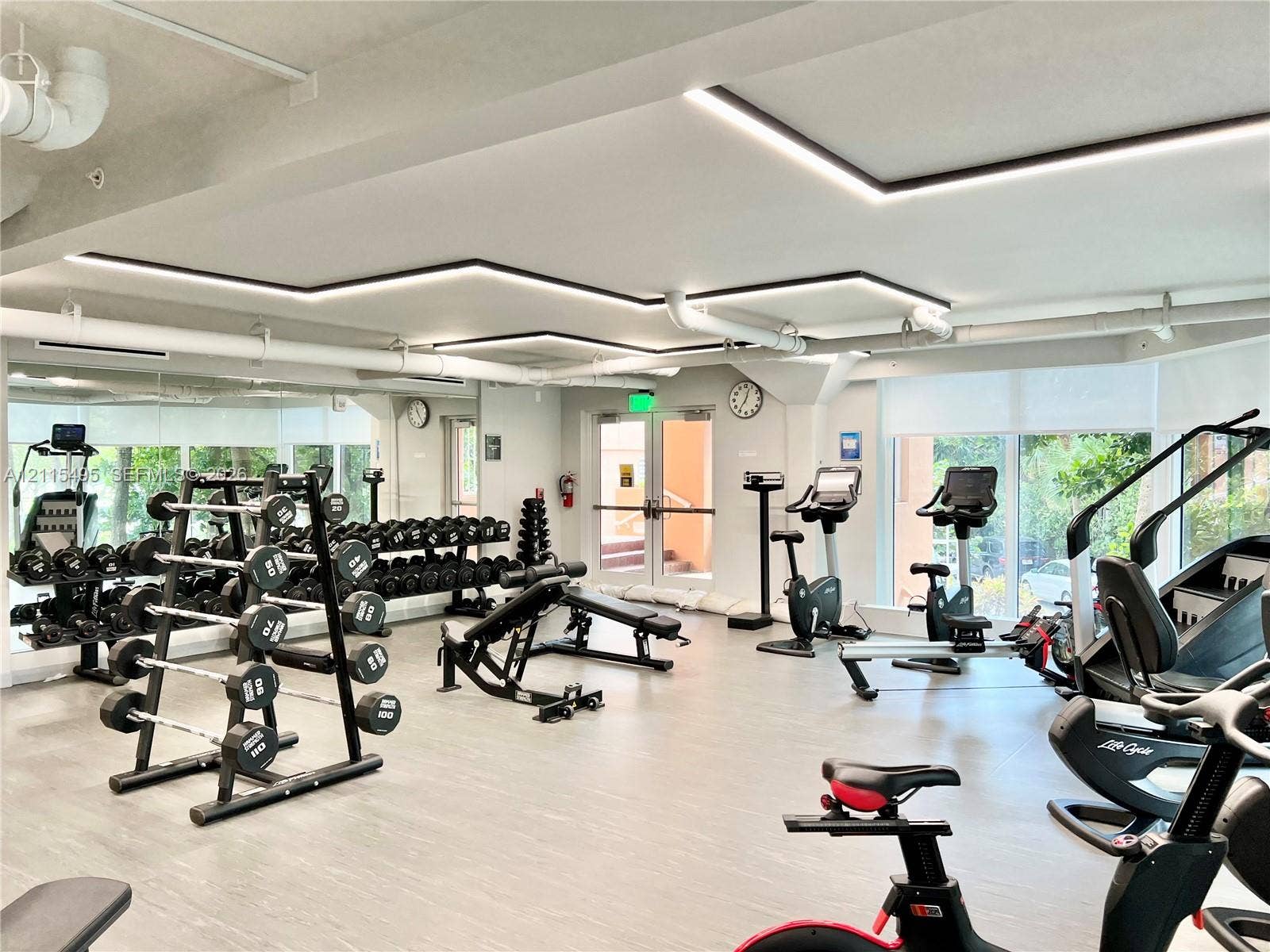 Fitness area featuring linear recessed LED ceiling lighting, full-wall mirrors, light-toned resilient flooring, and expansive windows