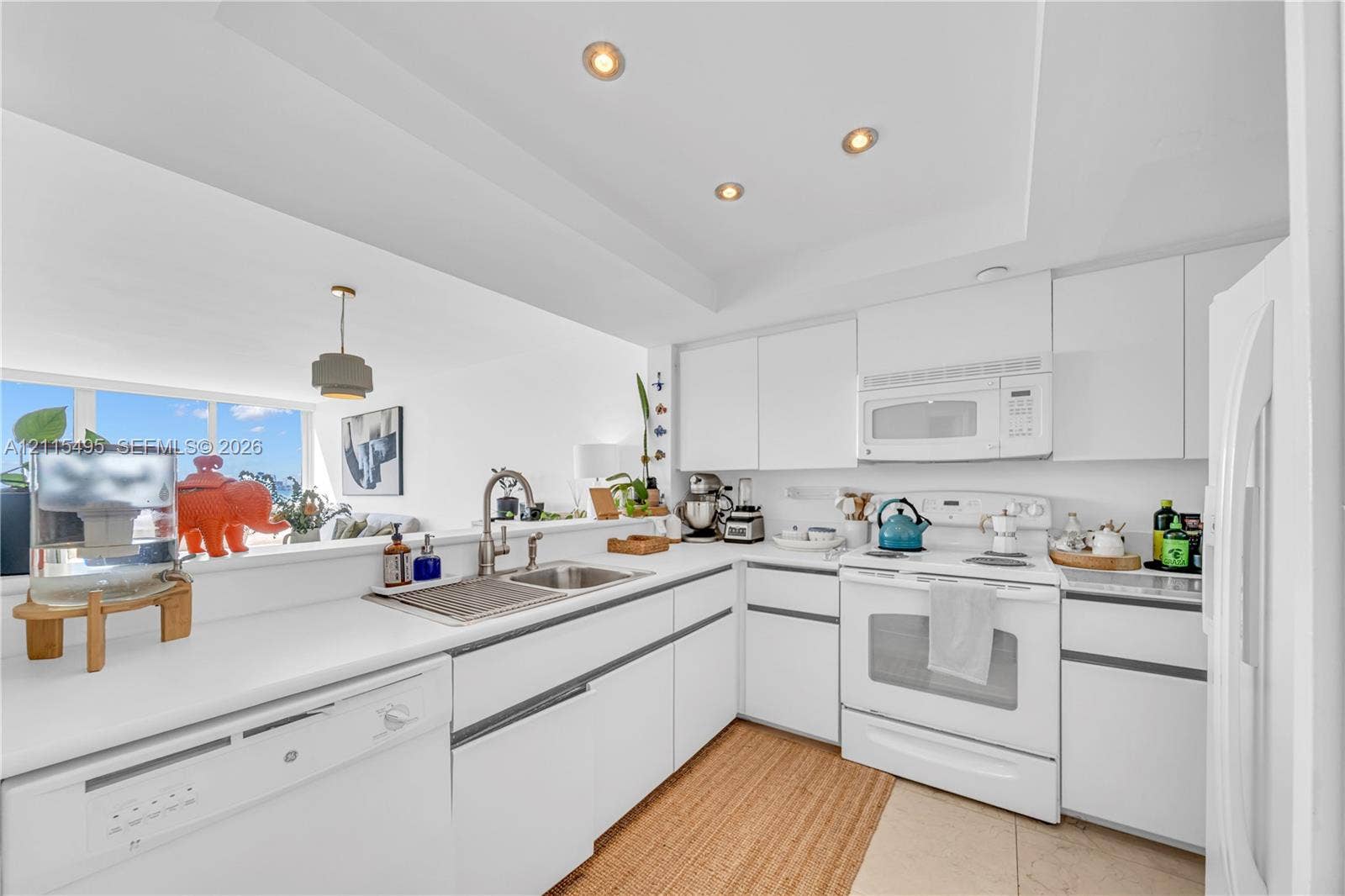 Kitchen featuring white flat-panel cabinetry, solid surface countertops, a stainless steel double-basin sink with a gooseneck faucet, and recessed ceiling lighting