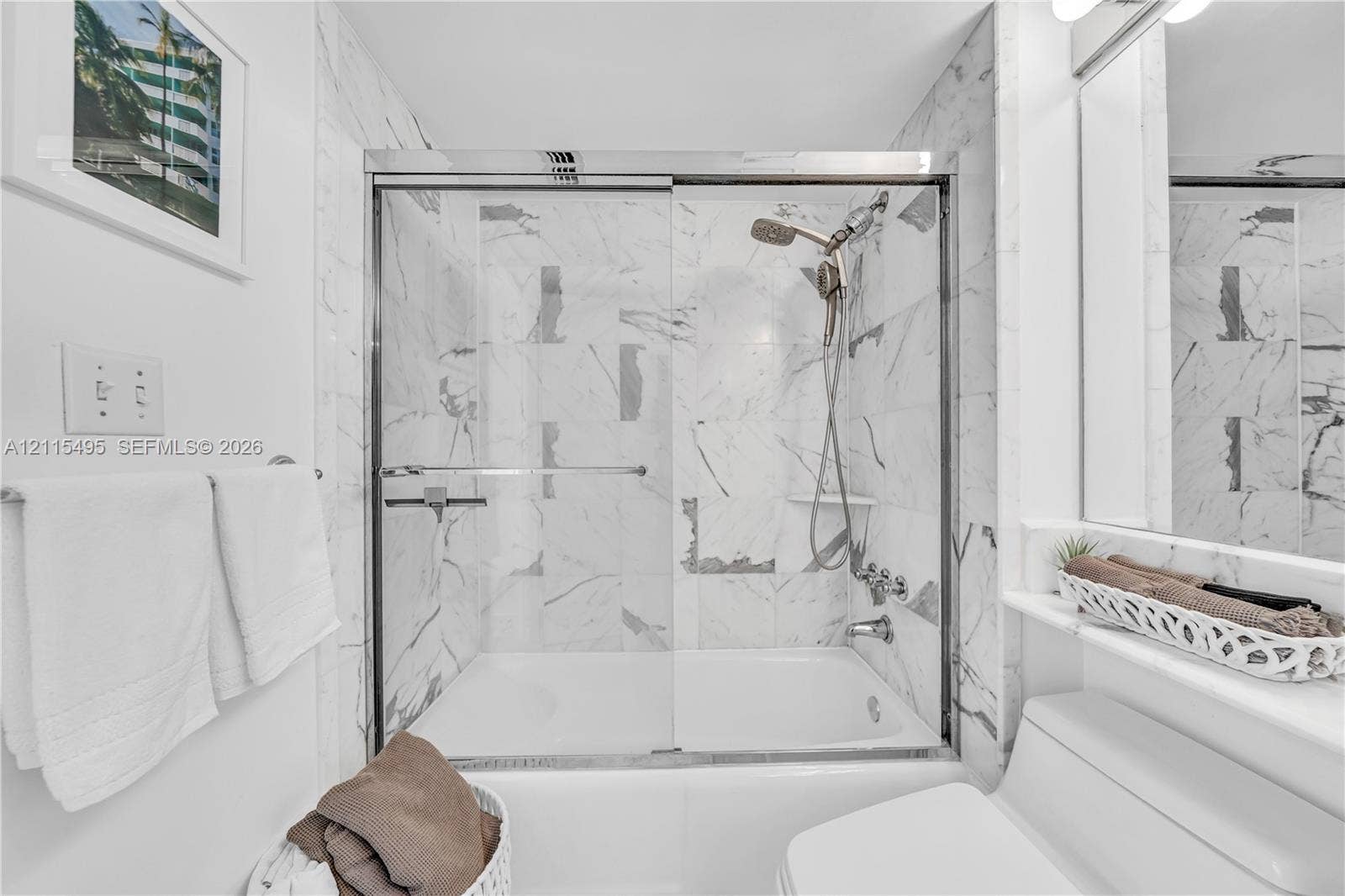 Bathtub and shower combination featuring full-height stone-patterned wall tile, a sliding glass enclosure, handheld shower hardware, and a built-in recessed shelf