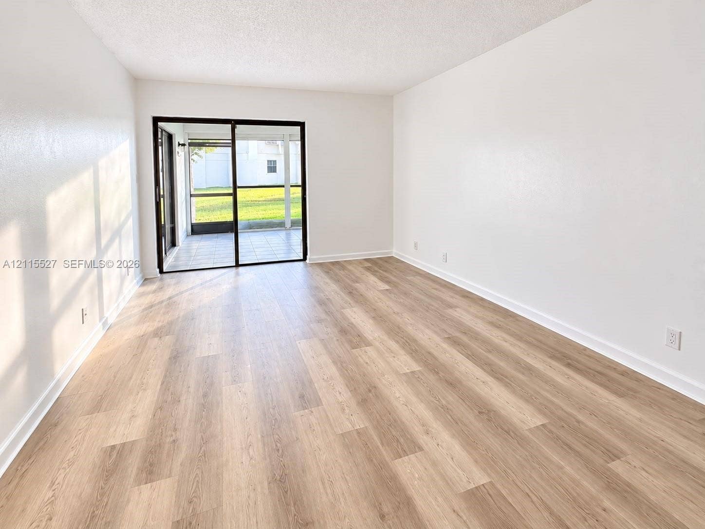 220 Lakeview Drive, #101, Weston, Weston, FL 33326 Interior space featuring neutral wall paint, wood-finish flooring, and a sliding glass door with black trim opening to a screened patio