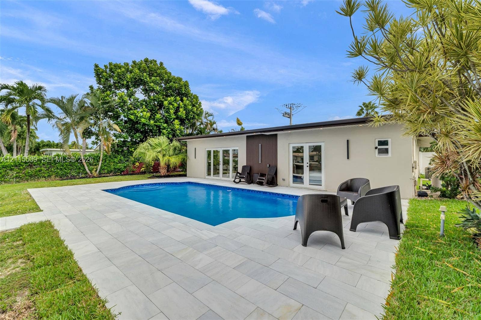 381 SE 6th Terrace, Pompano Beach, FL 33060 In-ground swimming pool with light-toned stone paver decking, exterior wall lighting, and double-glass door entry