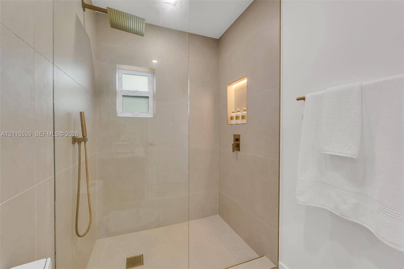 381 SE 6th Terrace, Pompano Beach, FL 33060 Walk-in shower featuring large-format wall tile, a frameless glass enclosure, a rainfall showerhead, a handheld sprayer in a metallic finish, and a recessed tiled niche with integrated lighting