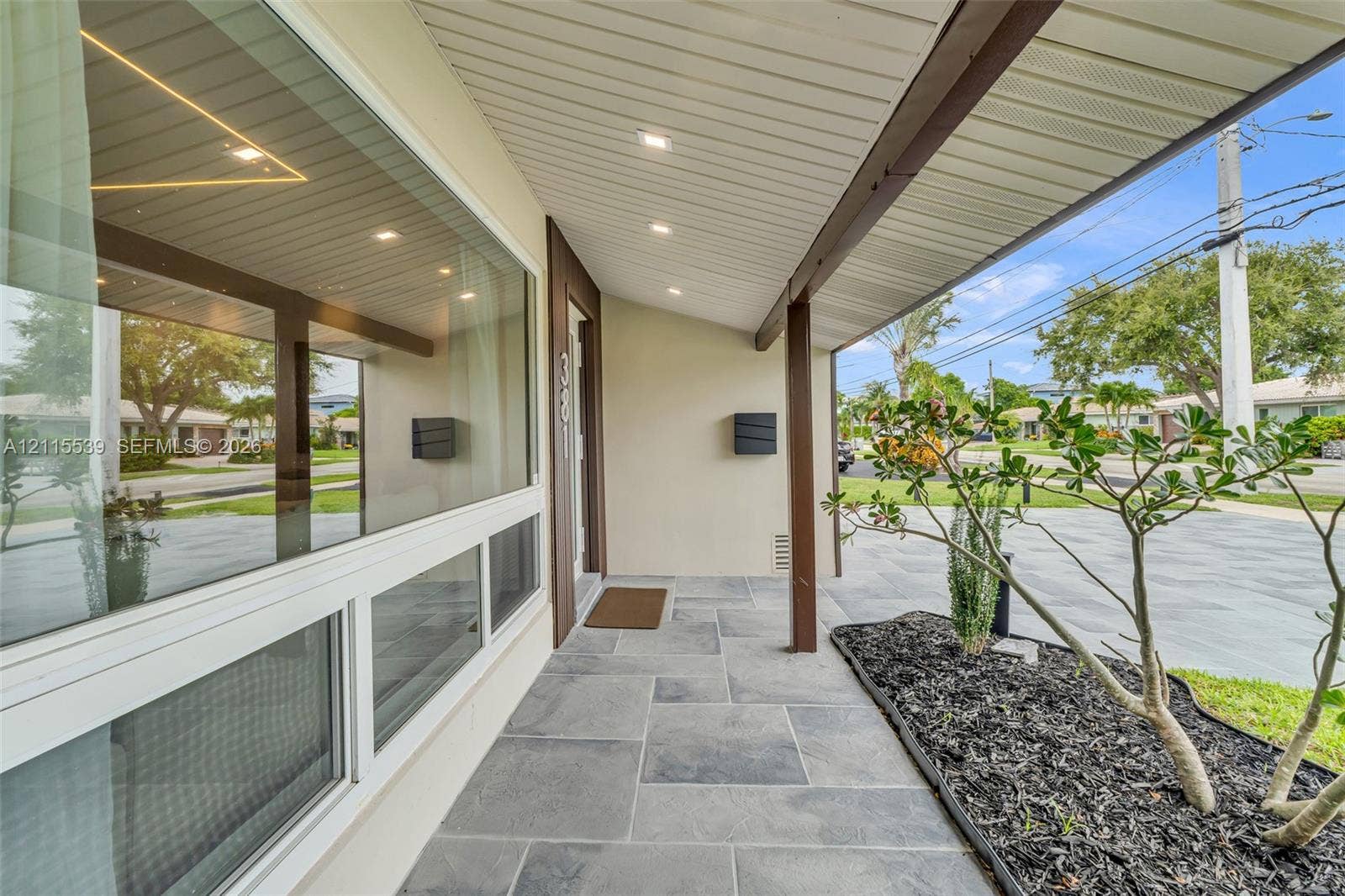 381 SE 6th Terrace, Pompano Beach, FL 33060 Covered entryway featuring large-format grey stone floor tiles, recessed ceiling lighting, a sprawling paneled window, and dark wood-finish structural support beams