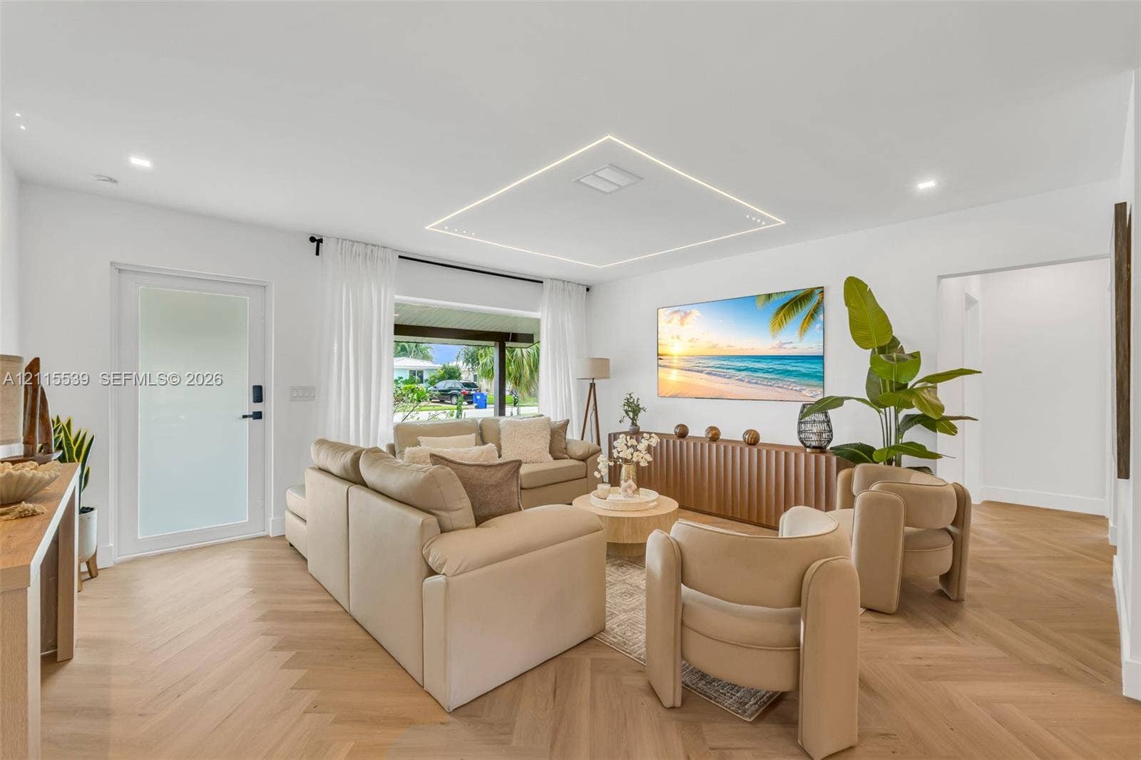 381 SE 6th Terrace, Pompano Beach, FL 33060 Living area featuring light-toned herringbone patterned flooring, recessed ceiling lighting, a recessed rectangular architectural ceiling detail with perimeter illumination, and a frosted glass entry door