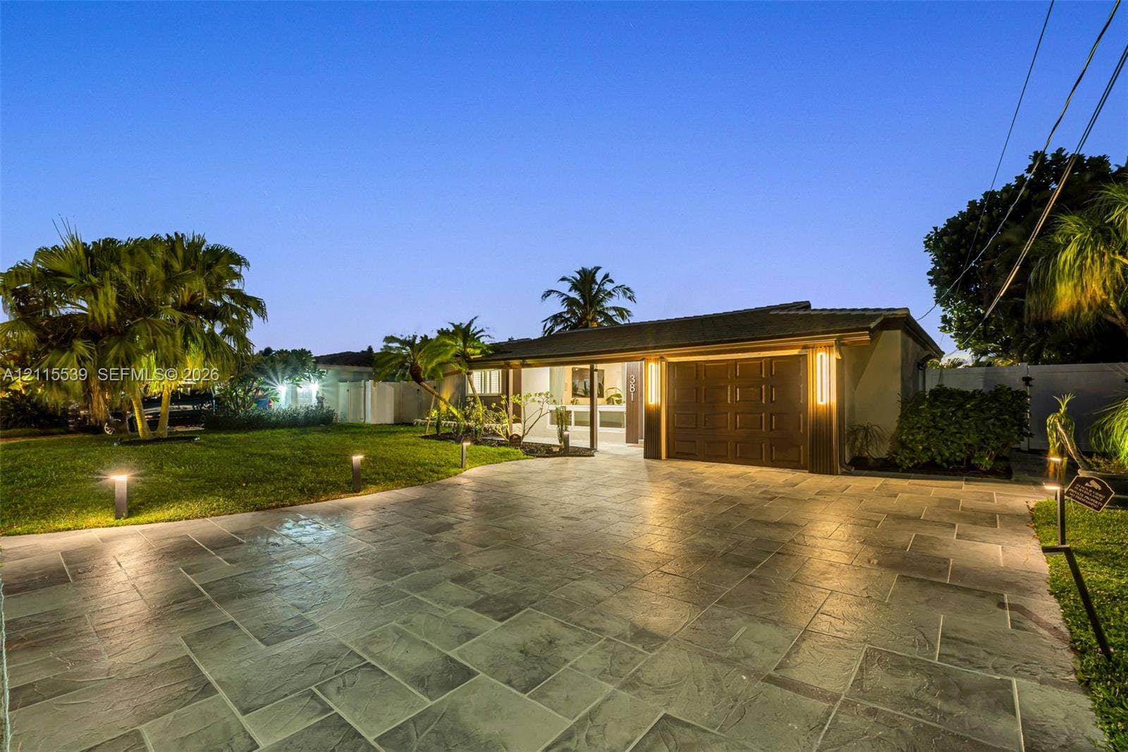 381 SE 6th Terrace, Pompano Beach, FL 33060 Single-story residence featuring a large stone-paver driveway, integrated garage, manicured lawn, and mature palm trees