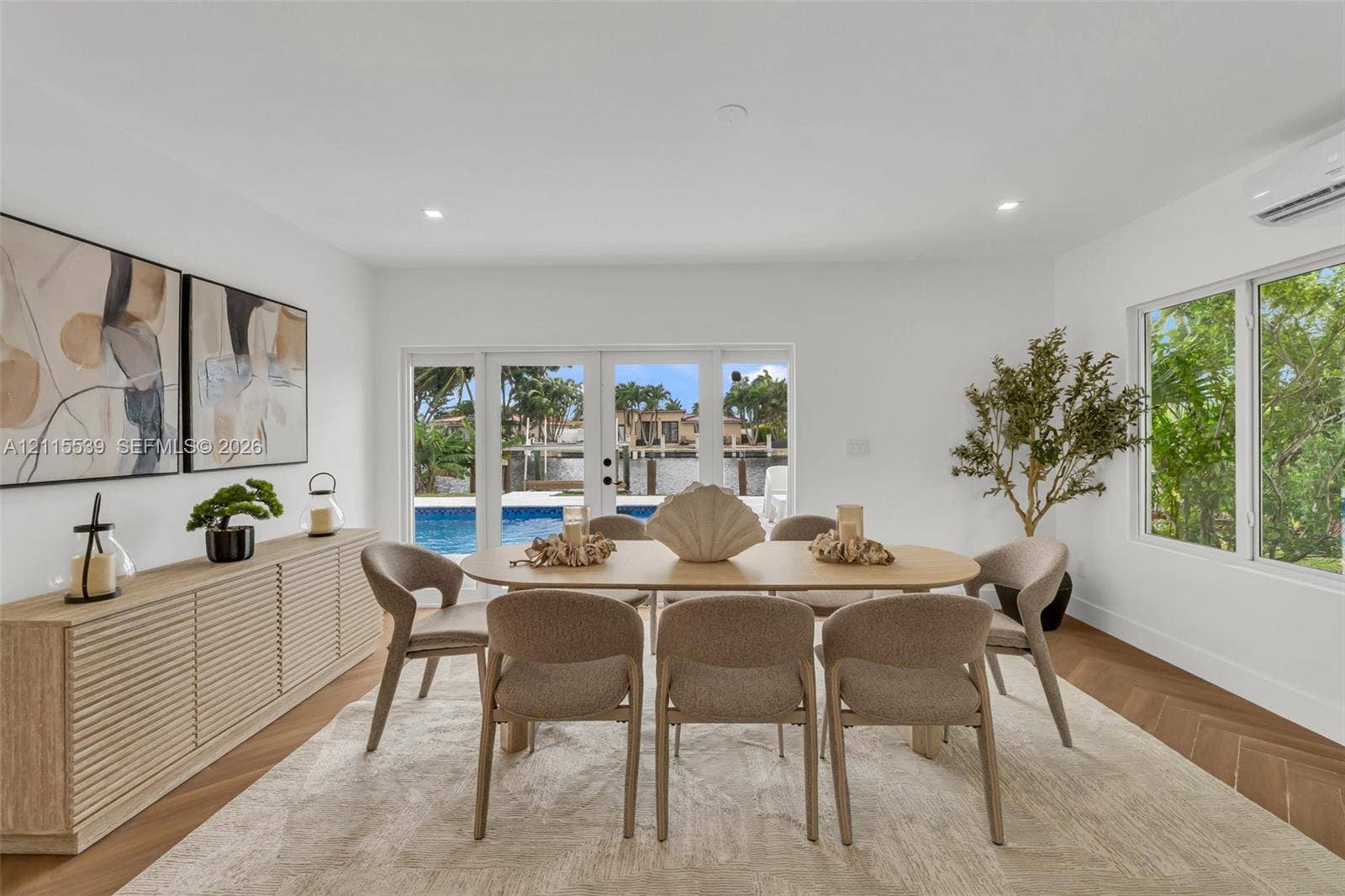 381 SE 6th Terrace, Pompano Beach, FL 33060 Herringbone-patterned wood-finish flooring, built-in slatted cabinetry, recessed ceiling lighting, and expansive glass paneled doors providing visibility to the pool area