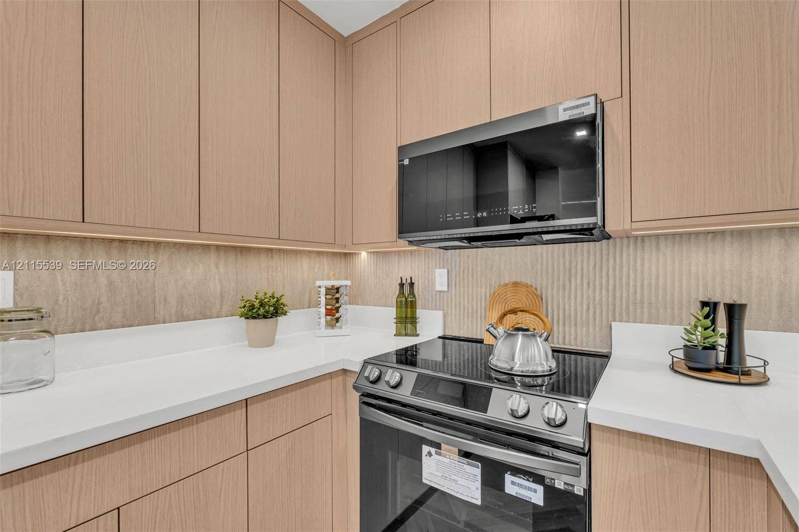381 SE 6th Terrace, Pompano Beach, FL 33060 Flat-panel light wood cabinetry featuring under-cabinet lighting, solid surface countertops, textured backsplash, and herringbone-pattern wood-finish flooring