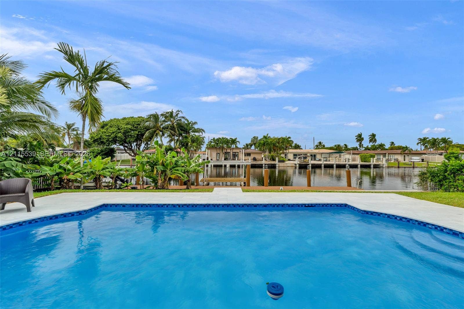 381 SE 6th Terrace, Pompano Beach, FL 33060 In-ground swimming pool with a concrete surround, dock, and bulkhead, bordered by mature palm trees and water frontage