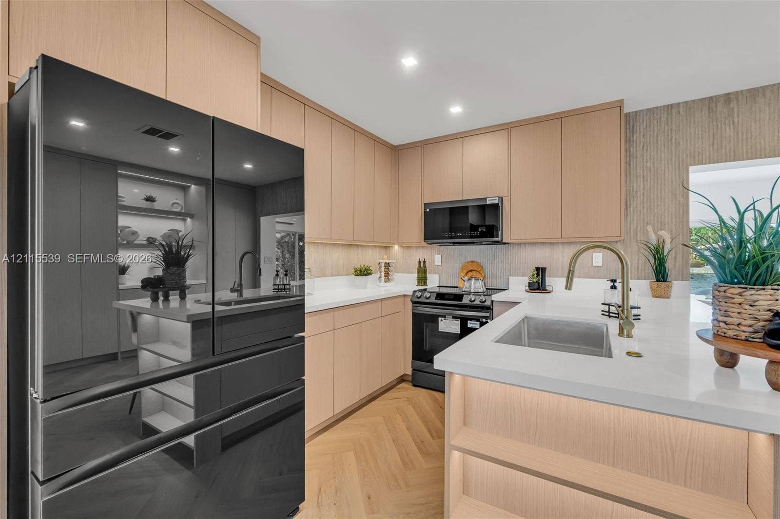 381 SE 6th Terrace, Pompano Beach, FL 33060 Kitchen featuring flat-panel wood cabinetry, light-toned stone countertops, herringbone-patterned wood flooring, integrated under-cabinet lighting, and a stainless steel undermount sink with a high-arch brass faucet