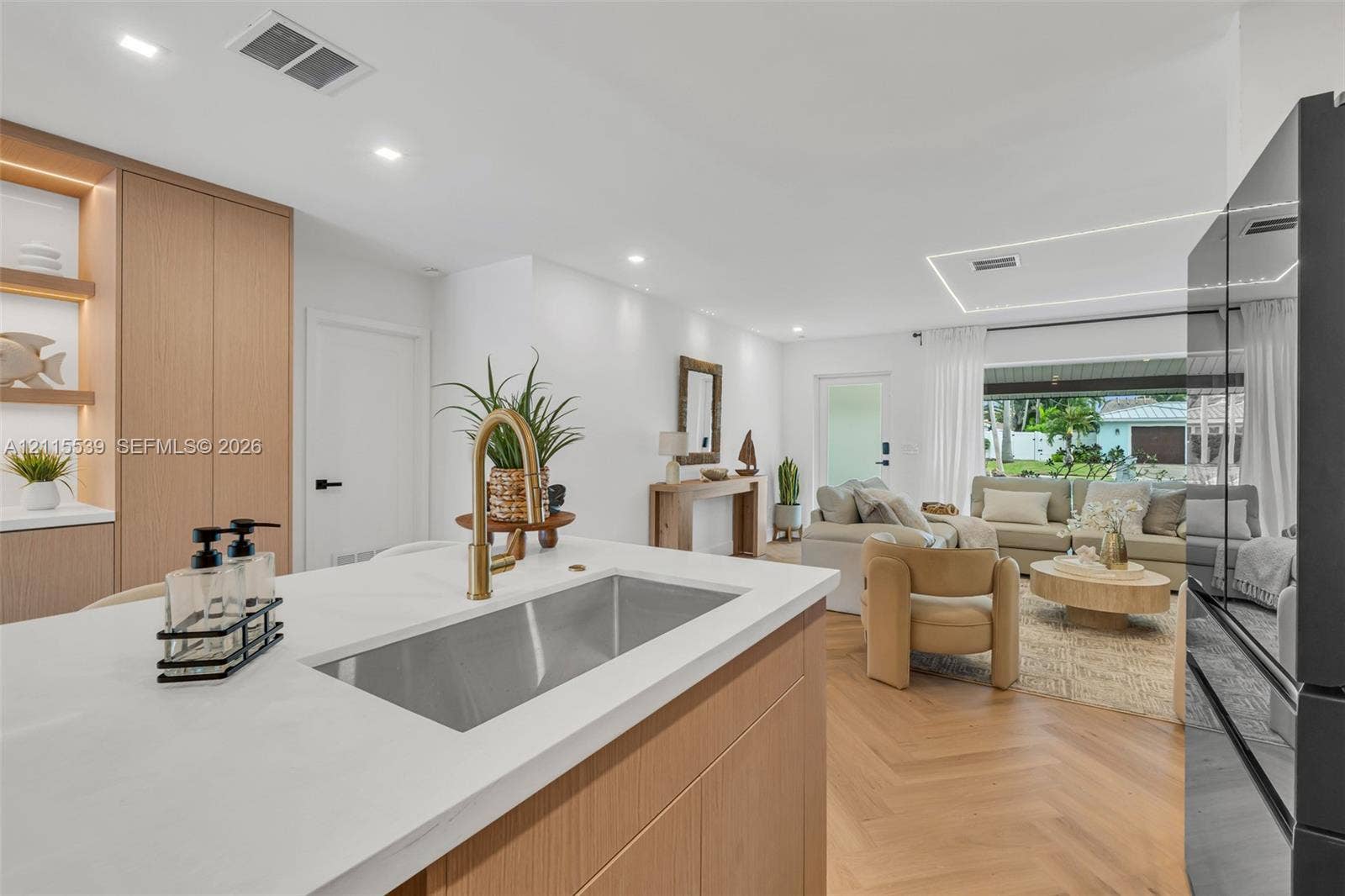 381 SE 6th Terrace, Pompano Beach, FL 33060 Kitchen island featuring a white countertop and stainless steel undermount sink with a brass-finish faucet, light wood-finish cabinetry, and chevron-pattern wood-finish flooring