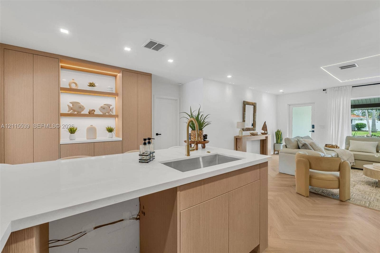 381 SE 6th Terrace, Pompano Beach, FL 33060 Kitchen featuring light wood-finish cabinetry, a white quartz countertop, an undermount stainless steel sink with a brass faucet, built-in recessed shelving with integrated lighting, and herringbone wood-finish flooring