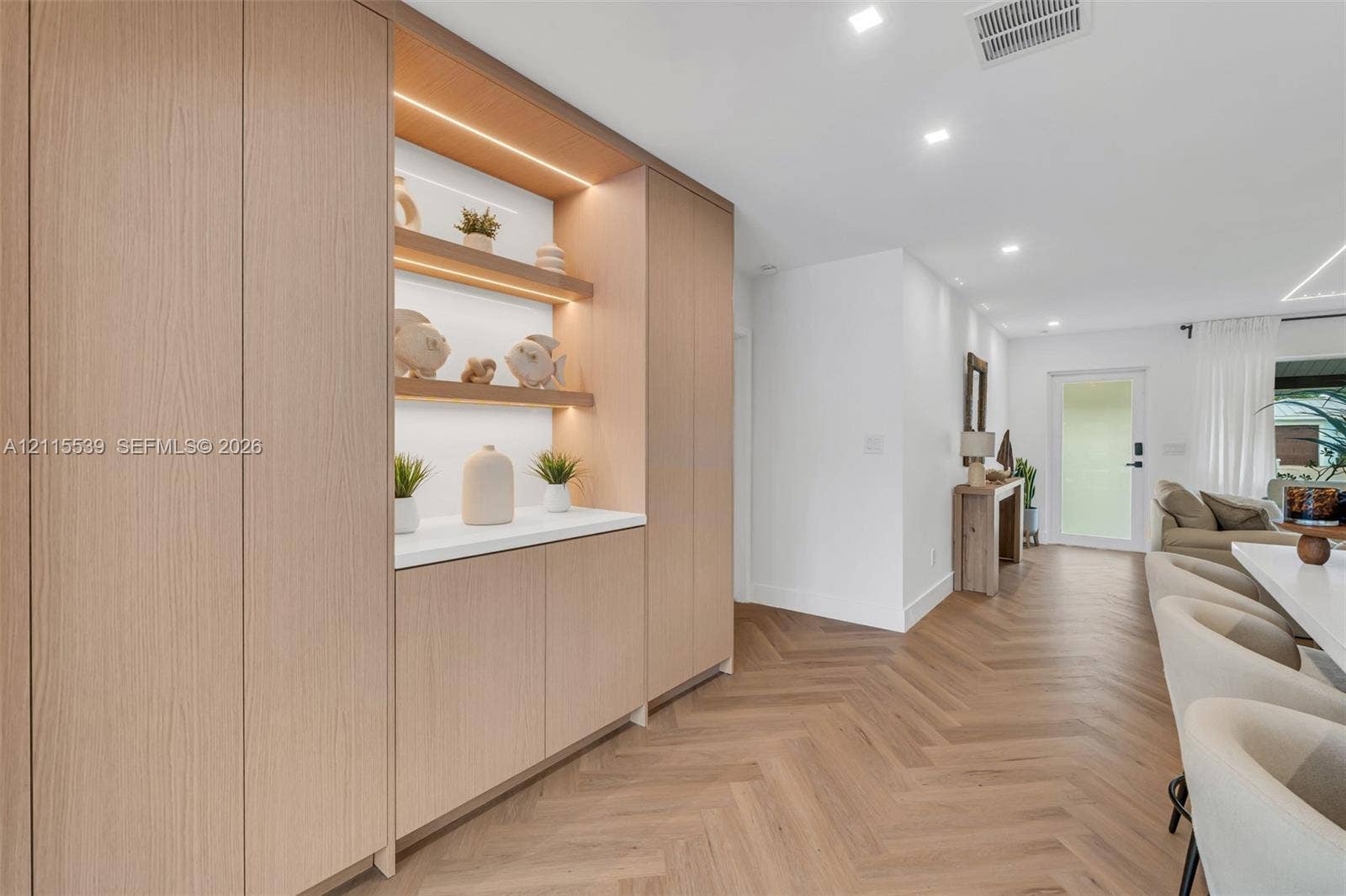 381 SE 6th Terrace, Pompano Beach, FL 33060 Custom floor-to-ceiling cabinetry featuring integrated LED display shelving, smooth-surface countertops, and light-tone wood finish flooring in a herringbone pattern